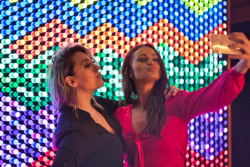 LiteZilla Giant Lite Brite 10' x 6' Light Wall, colorful illuminated wall with two women taking selfies in front of it.