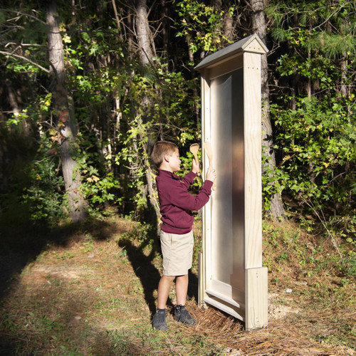 Wood Designs Outdoor Thunderwall, a wooden outdoor musical instrument for kids, in a natural outdoor setting with a young boy playing with wooden percussion instruments.
