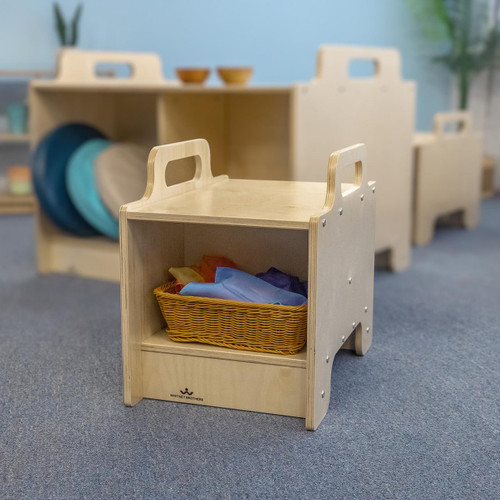 Whitney Brothers Stack-Able™ Seat, wooden modular children's seating with a basket of colorful fabrics inside, in a classroom setting.
