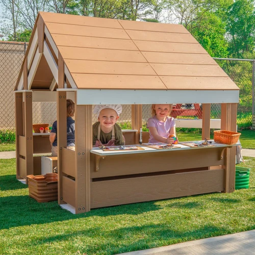 Whitney Brothers outdoorED™ Learning Pavilion, children playing and engaging in activities in a wooden outdoor playhouse with a roof, surrounded by greenery and a fenced yard.