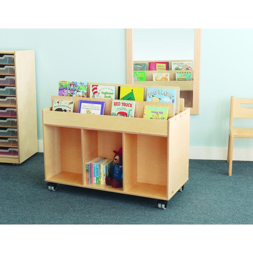 Whitney Brothers Mobile Book Storage Island, wooden mobile book storage unit with wheels holding children's books and a plush toy in a colorful classroom environment.