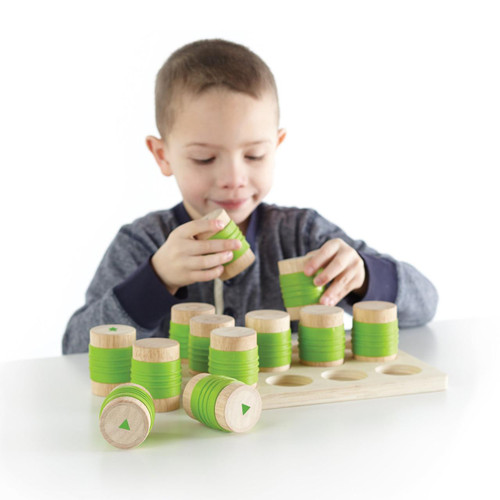 Guidecraft Weight Cylinders for Kids, a young boy playing with stacking and weight measurement wooden cylinders with green rings on a white table.