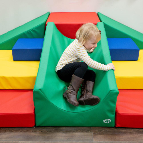 Children's Factory Highlands Soft Play Climber, a colorful foam climbing structure with a green slide, red platform, blue step blocks, and yellow base, being played on by a young child.