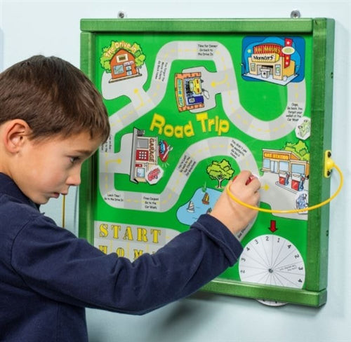 Playscapes Road Trip Magnetic Wall Activity, a child interacting with a green magnetic activity board featuring a colorful route map and various cityscape illustrations.
