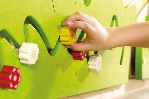 HABA Pro Blooming Meadow Wooden Play Wall Decoration, a child's hand adjusting colorful wooden knobs on a green play wall.