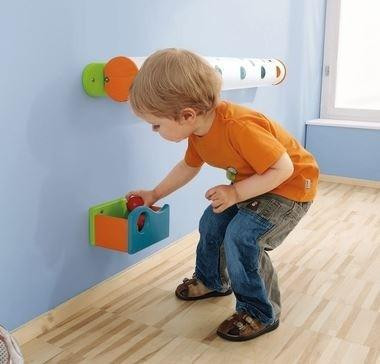 HABA Pro Marble Wall Track Catch Bin, a child playing with the colorful wall-mounted marble track system and catch bin in a room.