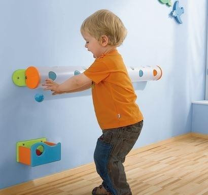 HABA Pro Marble Wall Track Catch Bin, a child playing with a wall-mounted marble track system with colorful catch bins and shelves.