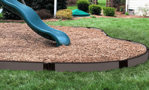 Frame It All Weathered Wood Curved Playground Border 16' - 1" Profile, garden playground edging with wood-like finish surrounding wood chip ground cover and a blue slide in a backyard.