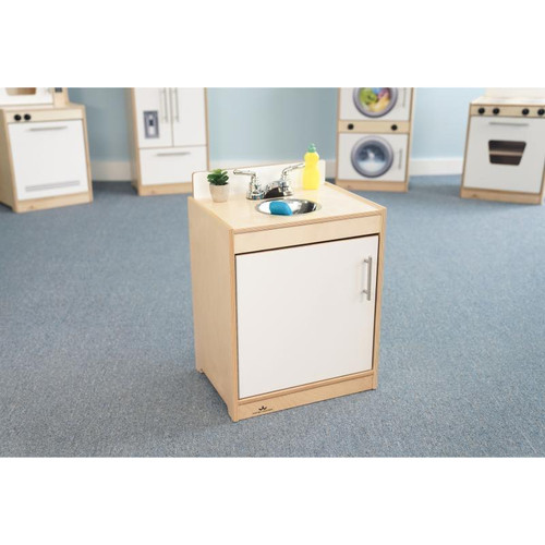 Whitney Brothers Contemporary White Kitchen Play Sink, wooden toy kitchen sink with white cabinet and stainless steel faucet, playroom setting with other miniature kitchen appliances in the background.