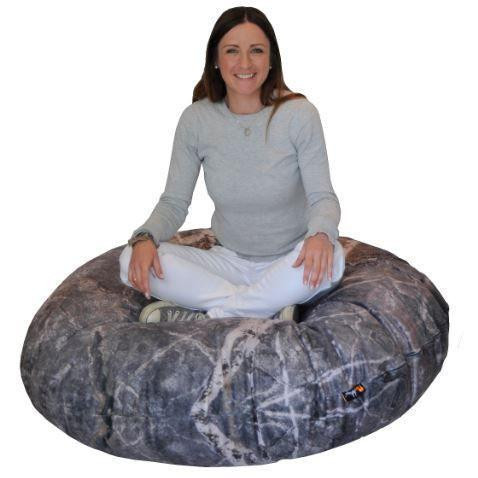 Playscapes Woodsmen Naturescape Stone Pod, a woman sitting cross-legged on a large, realistic stone-printed outdoor bean bag chair.