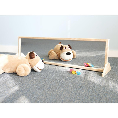 Whitney Brothers Vertical Or Horizontal Kids Mirror With Stand, plush dog toy and colorful toys on a gray carpeted floor, reflective mirror with wooden frame.