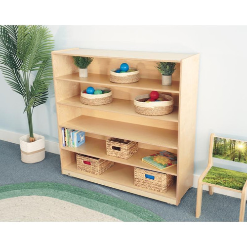 Whitney Brothers Mobile Bookshelf Cabinet 48H, a light wood shelving unit with baskets and books, in a well-lit room with a potted plant and a chair with a nature scene on the seat.