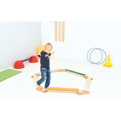 Moje Bambino Snake Balance Board, a child balancing on an elongated wooden balance board in a playroom with colorful sports equipment.