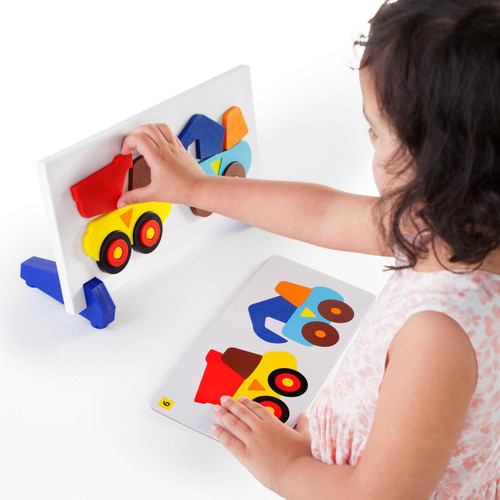 Guidecraft Construction Truck Sort and Match Game, a child's hand placing colorful wooden truck pieces onto a white matching board.