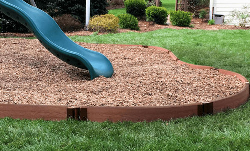 Frame It All Classic Sienna Curved Playground Border Border 16' - 1" Profile, brown plastic garden border with a curved shape surrounding a children's playground area with wood mulch and a blue slide in a backyard garden.
