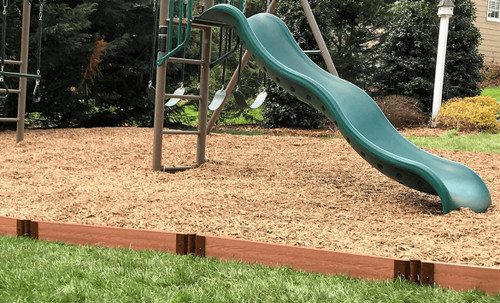 Frame It All Classic Sienna Straight Playground Border 16' - 2" Profile, brown wooden garden edging surrounding a playground area with green grass, a slide, and swing set in the background.
