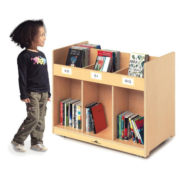Whitney Brothers Mobile Library Book Cabinet, wooden bookshelf with labeled sections for children's books, positioned against a white background with a young girl looking at it.