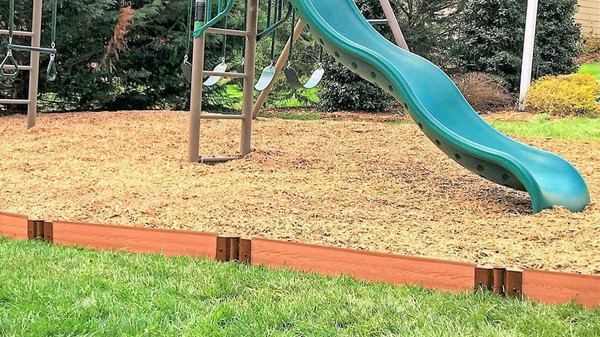 Frame It All Classic Sienna Straight Playground Border Kit 64' - 1" Profile, image of brown wooden border kit installed around a children's playground area with swing set and slide.