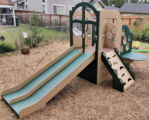 Strictly For Kids Deluxe Challenger 25 Wave Style Playground Structure, natural and bright colored slide and climbing walls set up in a backyard with wood chip ground covering.