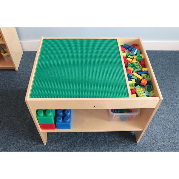 Whitney Brothers Construction Site Activity Table, wooden play table with a green LEGO baseplate on top and colorful building blocks on the side and shelf.