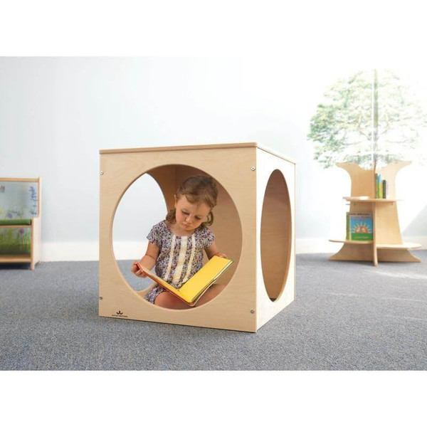 Whitney Brothers Toddler Playhouse Cube, a child sitting inside a wooden playhouse cube with circular openings, engaging in reading a yellow book.