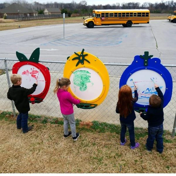 Infinity Playgrounds Fruit Outdoor Art White Board Activity Panels, children drawing on colorful fruit-shaped whiteboards outside near a school bus.