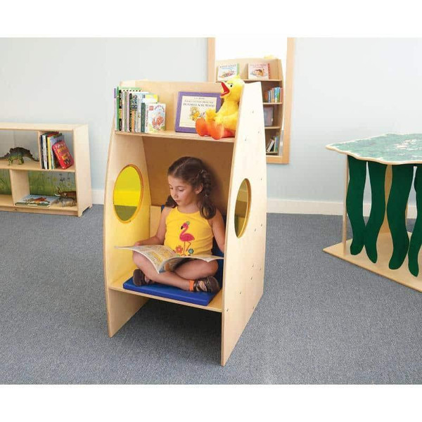 Whitney Brothers Alone Zone Reading Pod with Built-in Bookcase, wooden children's reading nook with a girl reading a book inside, featuring circular cut-out windows and a storage shelf for books.