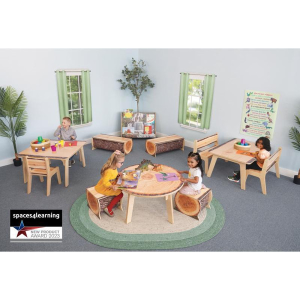 Whitney Brothers Nature View Live Edge Round Table 18" H, a children’s classroom with kids playing at a wooden round table with live edge sides, surrounded by matching wooden chairs, with colorful educational posters and plants in the background.