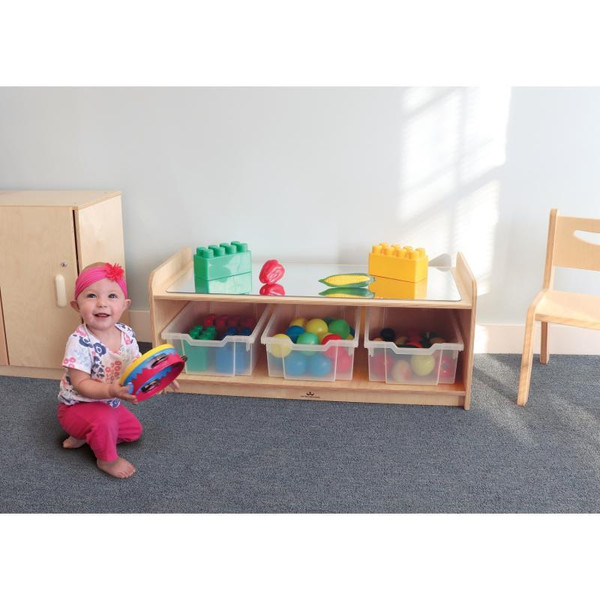 Whitney Brothers Toddler Play Table With Mirror Top, a wooden toddler play table with a mirror top and storage bins filled with colorful toys and building blocks, in a brightly lit playroom with a child playing nearby.