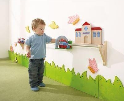 HABA Pro Push Along Train Rail Wall Activity, young boy playing with a wooden train set on a wall-mounted rail in a colorful playroom.