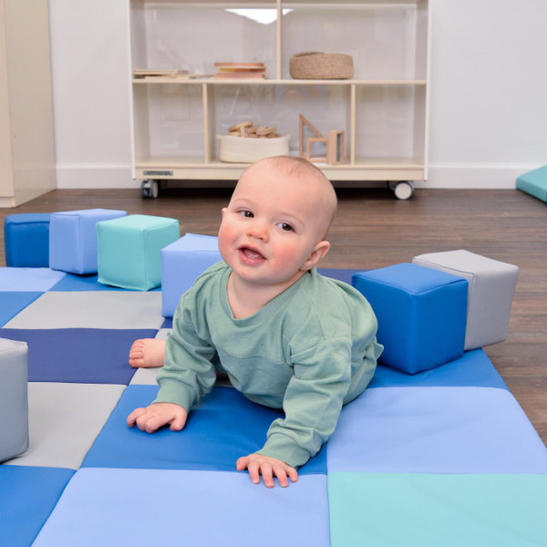 Children's Factory Patchwork Activity Mat & Foam Block Set, Tranquility, featuring a young child playing on a colorful padded foam mat with soft foam blocks in blue and gray, in a playroom setting.