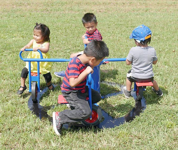 Infinity Playgrounds Infinity Mini Cycle Carousel with Pedal Track, children playing on the blue and red multi-person mini cycle with pedal track outdoors