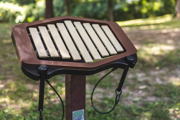 Freenotes Rhythm Outdoor Marimba, outdoor percussion instrument with wooden bars and metal resonators on a stand in a natural park setting.