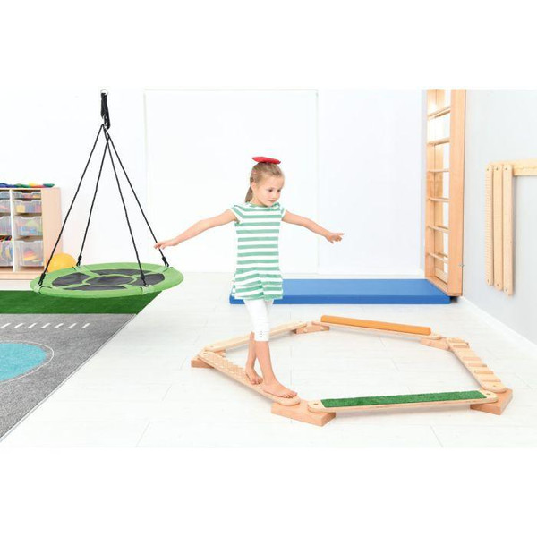 Moje Bambino Pillow Balance Board, a young girl balancing on a wooden and green pad within a playroom.