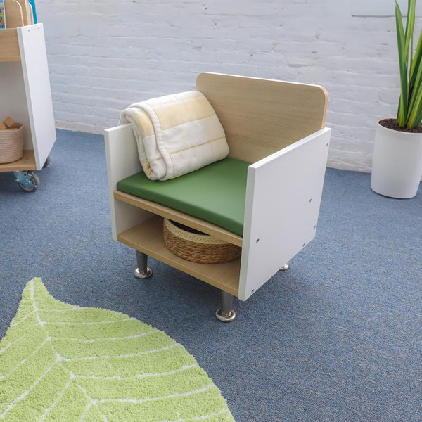 Whitney Brothers elevatED Children's Arm Chair, modern children's arm chair with a wooden backrest, white sides, green seat cushion, and a blanket draped over it, in a classroom setting.