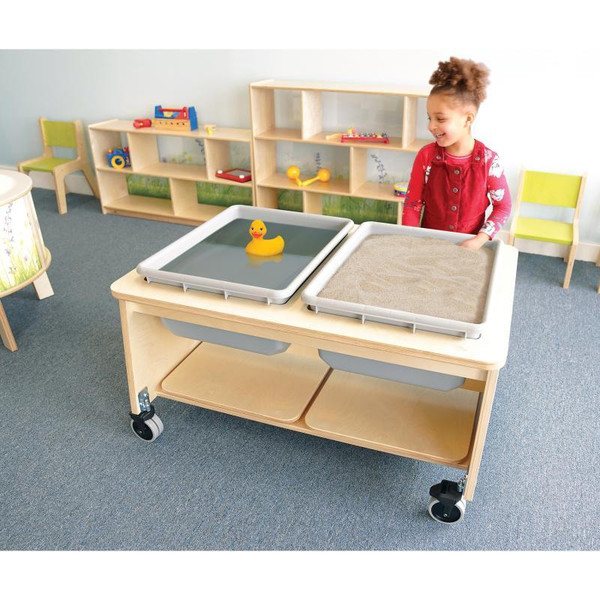 Whitney Brothers Whitney Plus Two Tub Sand And Water Table, a wooden educational table with two tubs, one filled with water and a rubber duck, in a classroom setting.