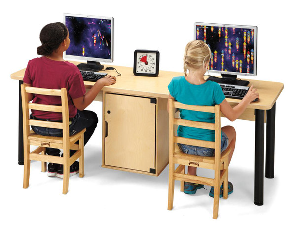 Jonti-Craft Dual Computer Lab Table, a classroom setting showing two children using computers at a shared wooden table with black metal legs, featuring a central cabinet for storage and a wall clock between the monitors.