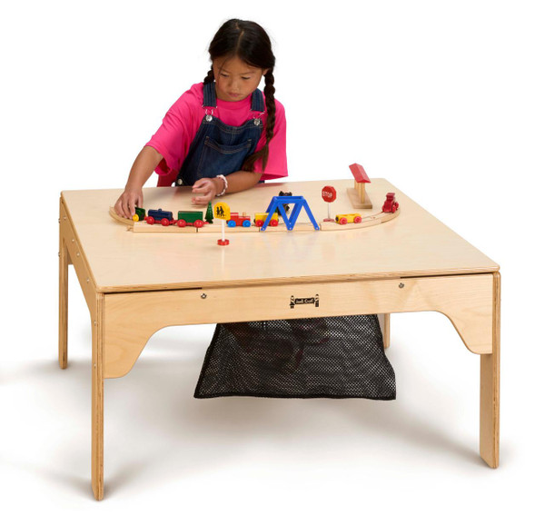 Jonti-Craft Large LEGO® and DUPLO® Square Table Cover, a child playing with wooden toy train set on a square wooden table with a natural finish and a black mesh storage bag underneath.