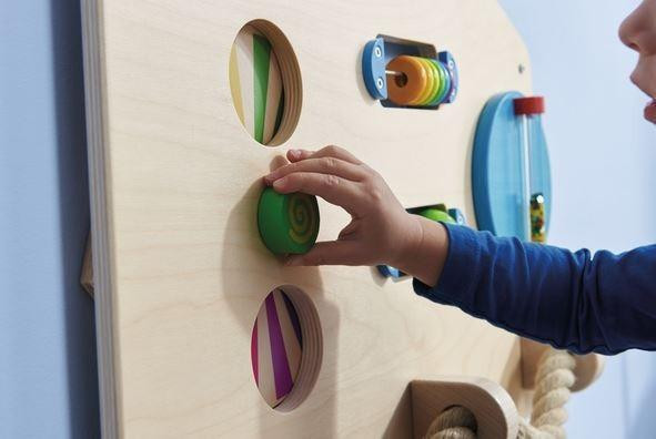 HABA Pro Motor Skills D Sensory Learning Wall Panel, child manipulating colorful wooden elements on an educational wall panel.