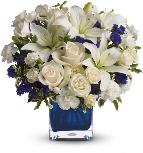 Send someone a bit of heaven with this beautiful bouquet. Luxurious cream roses and pure white lilies paint a peaceful picture inside a sapphire blue cube.  This arrangement is designed in a cube vase. These vases area about 4 1/2 inches square. They are tinted clear glass and are NOT dishwasher safe.