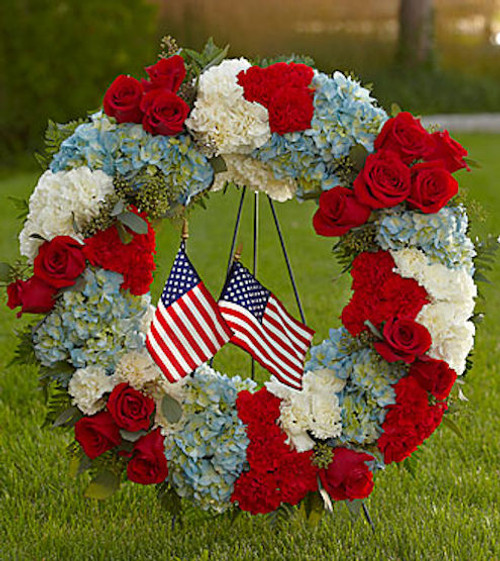 Pay tribute to a life lived in devotion and service to country with a red, white and blue floral wreath embellished with the beloved stars and stripes. A fitting way to celebrate the life of a veteran, government worker or any American patriot, this beautiful, full ring of colorful flowers includes red roses, red and white carnations and blue hydrangeas, beautifully complemented by lush greens. It adds a tasteful salute of patriotism on a floor-standing easel at a wake, for funeral services and for graveside burial services. Approximately 28"H x 24"W.