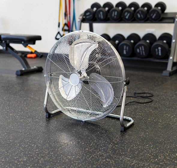 20 inch chrome floor fan on rubber gym floor next to weights rack and workout equipment