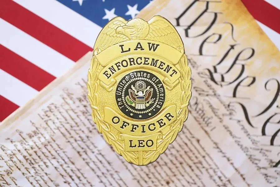 Gold law enforcement officer badge over an American flag and the Constitution