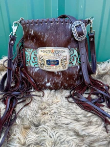 Brown cowhide buckle bag with white spots, fringe, and turquoise floral accent