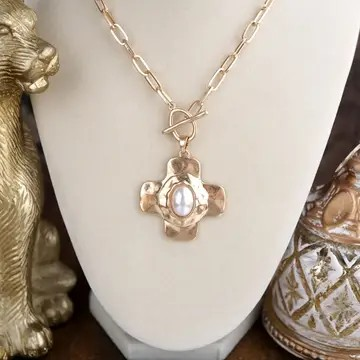 Hammered gold cross necklace with a luminous pearl-inspired center stone on a paperclip chain.