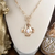 Hammered gold cross necklace with a luminous pearl-inspired center stone on a paperclip chain.