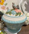 Elevate your kitchen decor with the Meadow Cookie Jar by Fitz and Floyd. Hand-painted with stunning detail, this ceramic earthenware jar from the Meadow Collection features a vibrant floral design and a charming bird perched atop the lid, bringing the freshness of spring to your home. Ideal for storing cookies, candy, sugar, coffee, and more, its removable lid ensures lasting freshness. Shop now for this elegant tabletop piece!