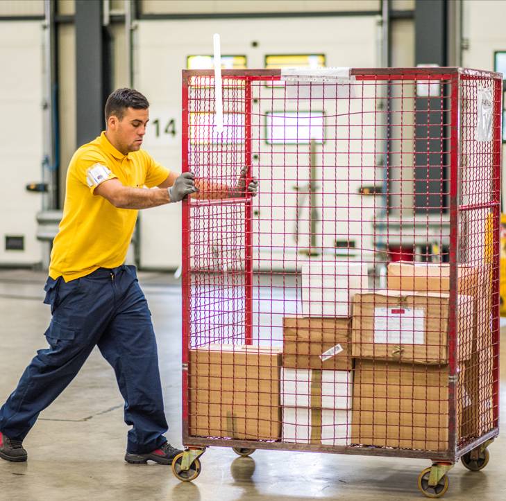 a man wearing a yellow shirt pushing a red cart full of packages with both hands