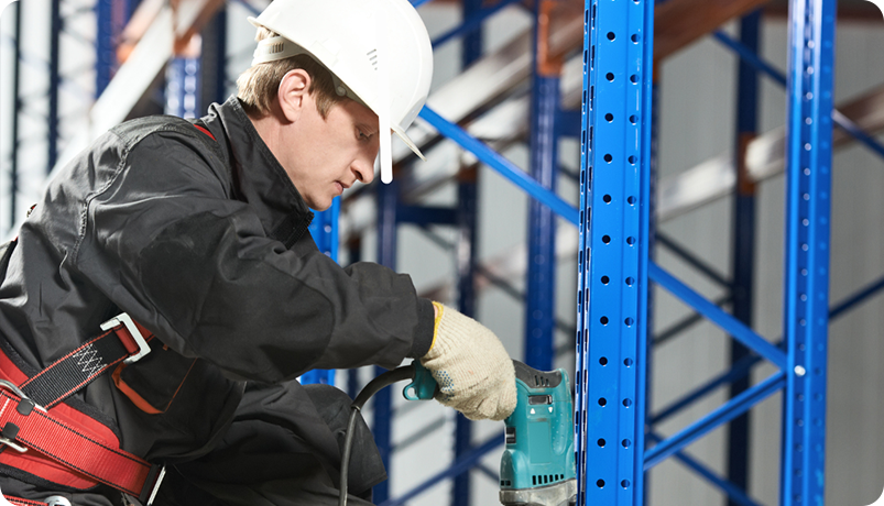 warehouse worker wearing safety equipment securing a rack with an electric screwdriver