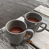 Two mugs of Vocoa hot cocoa on a dock.